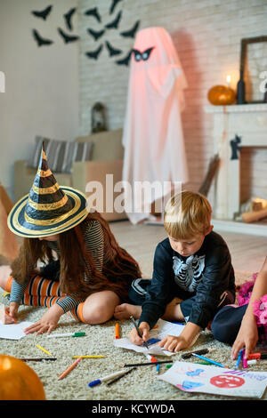 Portrait of three children wearing Halloween costumes drawing sitting on floor in decorated studio Stock Photo