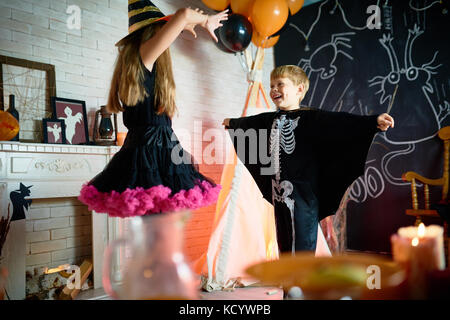 Cheerful children wearing Halloween costumes holding rehearsal before taking part in trick-or-treating, interior of decorated room on background Stock Photo