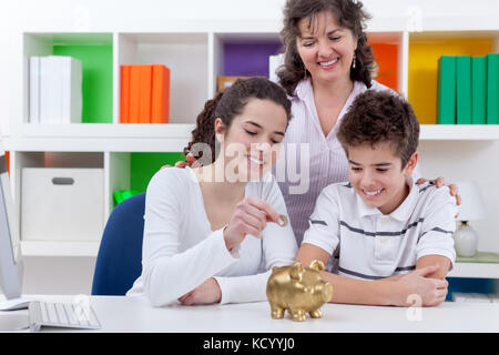 mother with her children putting money in piggybank, family saving Stock Photo
