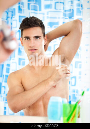young handsome man applying antiperspirant and looks at himself in mirror Stock Photo