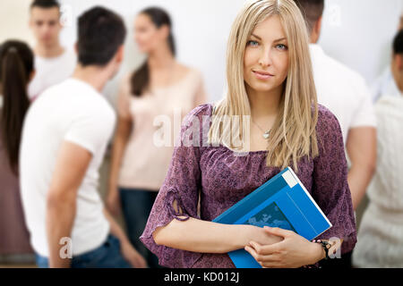 female student holding notebooks with colleagues students in background Stock Photo