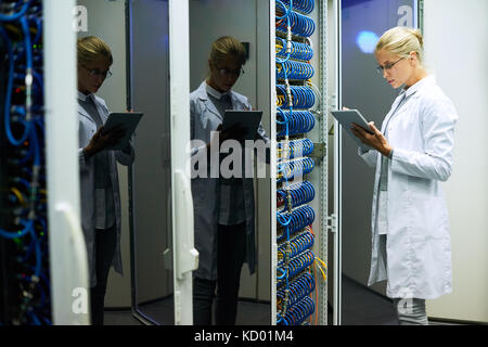 Side view portrait of beautiful young woman wearing lab coat  working with supercomputer inputting data to digital tablet Stock Photo
