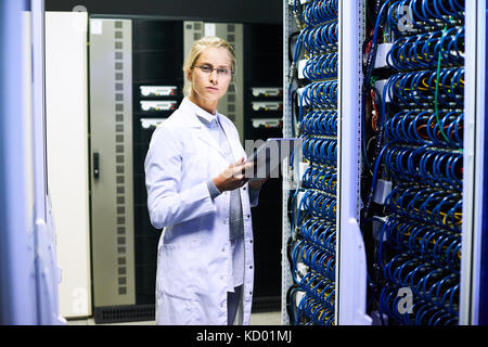 Side view portrait of young woman wearing lab coat  looking at camera while working with supercomputer Stock Photo
