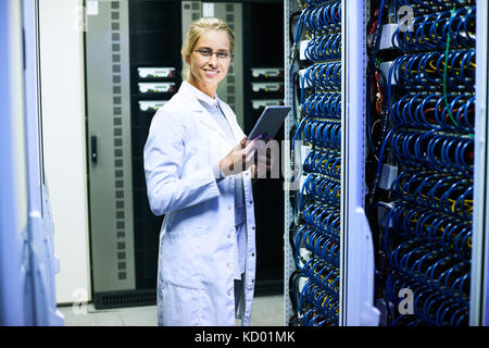 Portrait of young woman wearing lab coat  smiling at camera while working with supercomputer Stock Photo