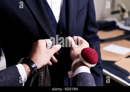 Closeup of tailor fitting bespoke suit to model, hands with tape measure and pin cushion fixing jacket on male model Stock Photo