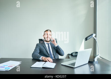 Portrait of successful business owner sitting at big desk in modern office speaking by phone  and laughing, copy space Stock Photo