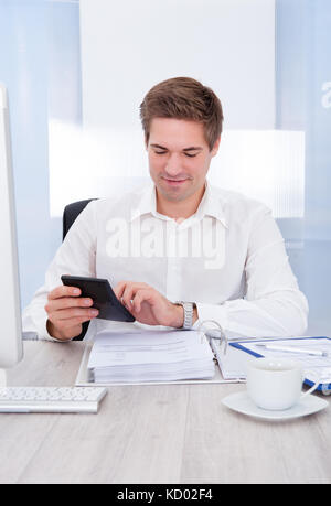 Happy Young Businessman Calculating Bills At Desk Stock Photo