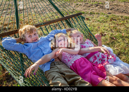 Three happy children swinging together on a hammock. Stock Photo