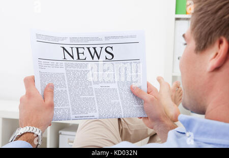 Happy Young Man Sitting On Couch Reading Newspaper Stock Photo