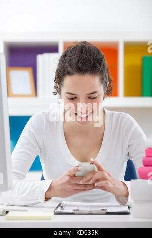 Smiling teenager girl using  phone while doing homework Stock Photo