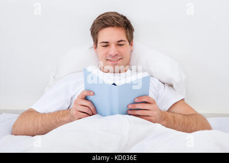 Happy Young Man Reading Book Lying On Bed Stock Photo