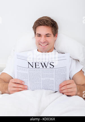 Man Relaxing On Bed While Reading Newspaper Stock Photo
