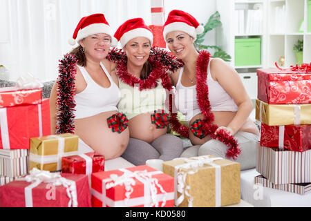 Three pregnant women with decorative bow on bellies, expecting babies for Christmas Stock Photo