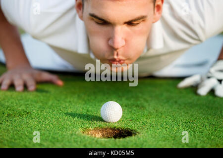 golfer lying on grass and blowing in the ball,  just need to give it a little help. Stock Photo