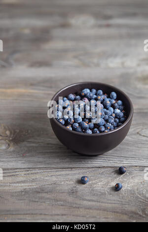 Small bowl with seeds of juniper on wooden table. Stock Photo