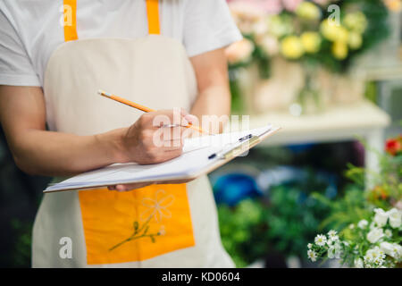 Cropped image of asian male florist making notes at flower shop counter Stock Photo