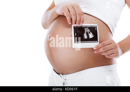 Pregnant woman holding ultrasound examination picture in front of her round belly, isolated on white background Stock Photo
