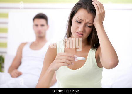 Upset woman looking in pregnancy test with her husband in background Stock Photo