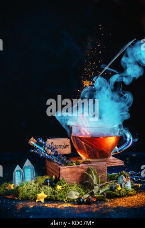 Magical still life with a tea cup, steam, flying vintage spoon, stardust, test tubes with potion ingredients, crystals and moss. Witch workplace concept. Stock Photo