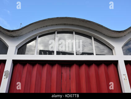Curvilinear roof and red concertina folding doors and glass window panes on Disused fire station with sky reflected in windows in Bury lancashire uk Stock Photo