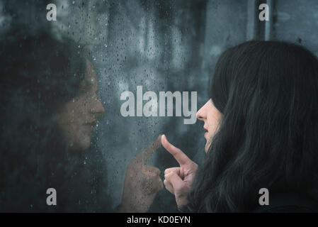 Young brunette woman looking through a window covered with raindrops and touching the glass with her finger Stock Photo