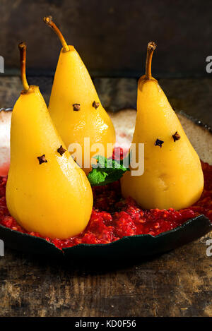 Pears poached in sweet syrup on crushed raspberries, presented as ghosts. Halloween food idea. Stock Photo