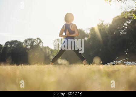 Mature woman in park, standing in yoga positions, hands behind back, rear view Stock Photo