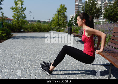 Young woman outdoors, doing push-ups on bench Stock Photo