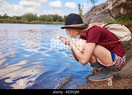 Woman crouching by waters edge scooping up water in hands, Krakow, Malopolskie, Poland, Europe Stock Photo