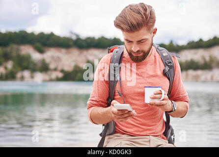 Man holding enamel mug using cellular phone, Krakow, Malopolskie, Poland, Europe Stock Photo
