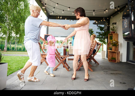 Senior and mature women dancing with female toddler at family lunch on patio Stock Photo