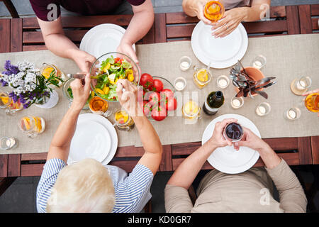 Overhead view of family handing salads at family lunch on patio Stock Photo