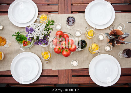 Overhead view of table prepared with flowers and vine tomatoes for lunch on patio Stock Photo