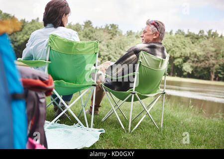 Mature couple sitting in camping chairs beside lake, rear view Stock Photo