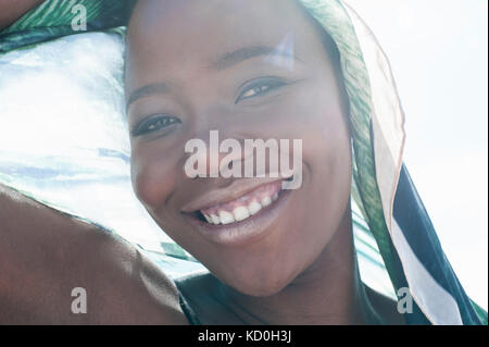 Portrait of young woman on beach, smiling, sheer scarf draped around her, close-up Stock Photo