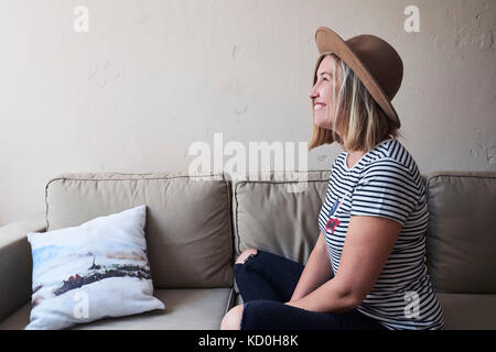 Woman sitting on sofa, smiling, side view Stock Photo
