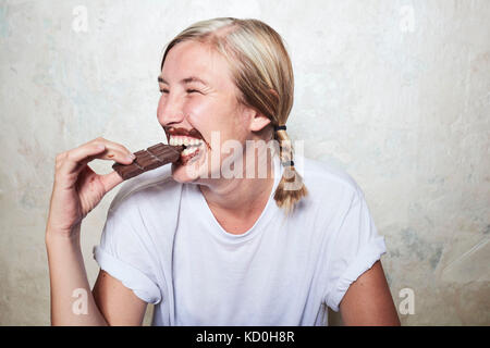Woman eating bar of chocolate, chocolate around mouth, laughing Stock Photo