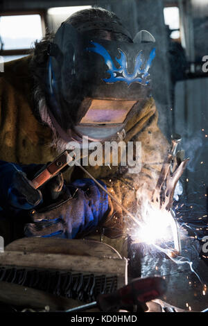Blacksmith in welding mask welding metal in workshop Stock Photo