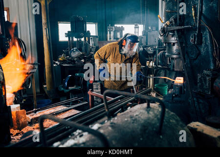 Blacksmith shaping red hot metal rod in workshop Stock Photo
