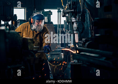 Blacksmith shaping red hot metal rod in workshop Stock Photo
