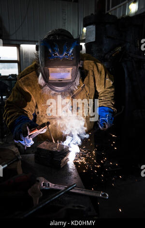 Blacksmith in welding mask welding metal in workshop Stock Photo