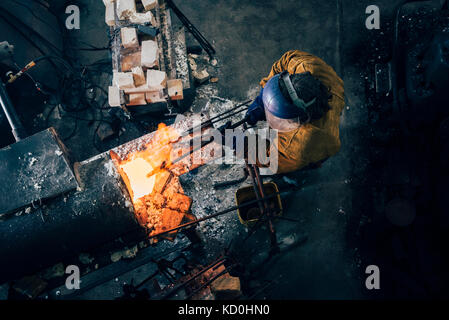 Overhead view of blacksmith shaping red hot metal rod in workshop furnace Stock Photo
