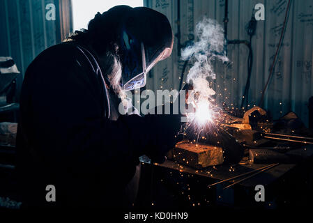 Blacksmith in welding mask welding metal in workshop Stock Photo