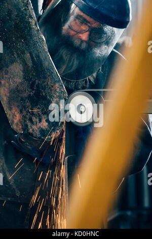 Blacksmith grinding metal on machine in metal workshop Stock Photo