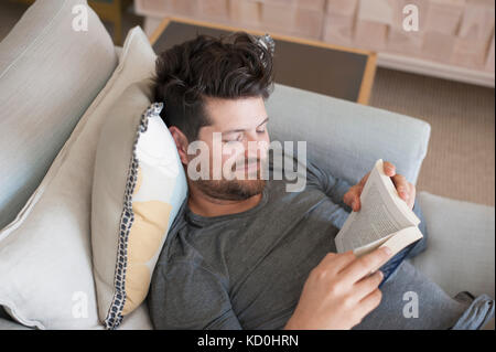 Mid adult man relaxing on sofa, reading book, elevated view Stock Photo