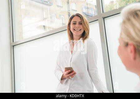 Businesswomen talking and using mobile phone in office Stock Photo