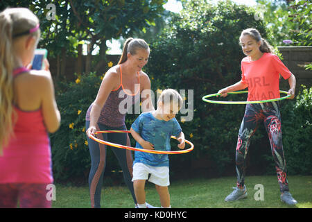 Girl photographing mother and siblings hoola hooping in garden Stock Photo