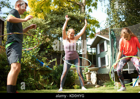 Mature couple and teenage daughter hula hooping in garden Stock Photo