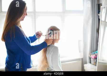 Mother brushing schoolgirl daughter's hair in bedroom Stock Photo