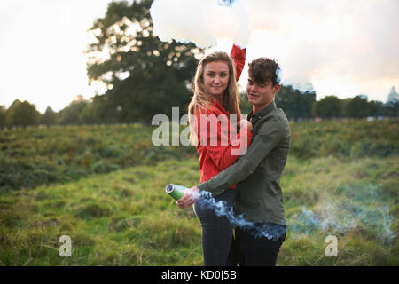 Young couple letting off smoke flares in field Stock Photo